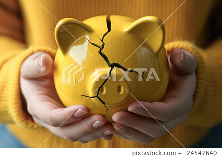 Person Holding a Yellow Piggy Bank with a Large Crack in It 124547640