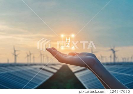 Human Hand Gently Holding Symbol of Hydrogen Energy with Wind Turbines in Background 124547650