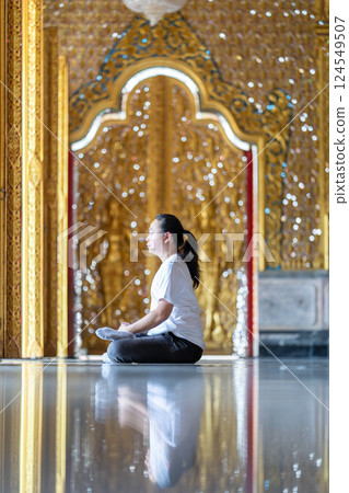 Asian Man meditates on the ground with reflection in the sunlight pouring into the temple church with gold gold Thai pattern blur background. Asian Man meditates on the ground with reflection in the sunlight pouring into the temple church with gold gold Thai pattern blur background. 124549507
