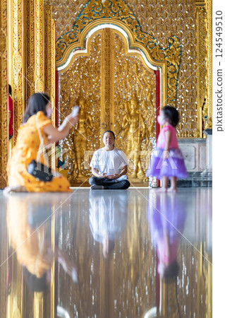 Asian Man meditates on the ground with reflection in the sunlight pouring into the temple church with gold gold Thai pattern blur background. 124549510