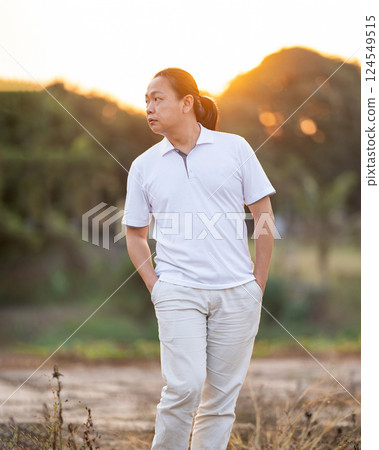 Asian Man long hair stands and relax on the dry field in golden twilight time. 124549515