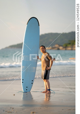 Smart Asian Man long hair touches and poses with Standed Surfboard on the beach in Twilight time 124549528