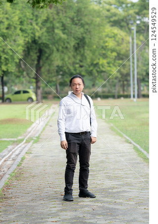 Asian freelance long hair man standing and posting on the walk way in the garden outdoor field with his camera beside him. 124549529