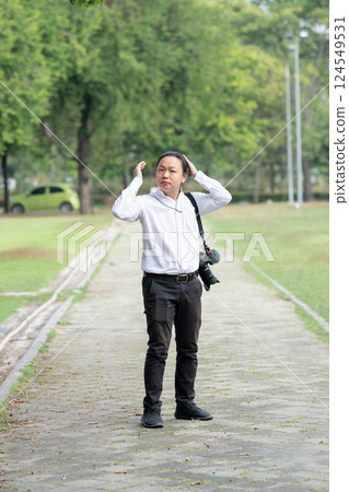 Asian freelance long hair man standing and posting on the walk way in the garden outdoor field with his camera beside him. 124549531