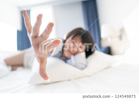 Abstract and Blurry Asian cute woman lying down on white pillow and bed then she raises up her hand to the camera. 124549873