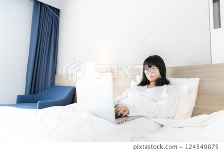 Glasses Asian cute woman works and plays laptop notebook on the bed in Work From Home period. Glasses Asian cute woman works and plays laptop notebook on the bed in Work From Home period. 124549875