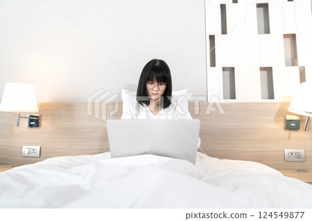 Glasses Asian cute woman works and plays laptop notebook on the bed in Work From Home period. Glasses Asian cute woman works and plays laptop notebook on the bed in Work From Home period. 124549877