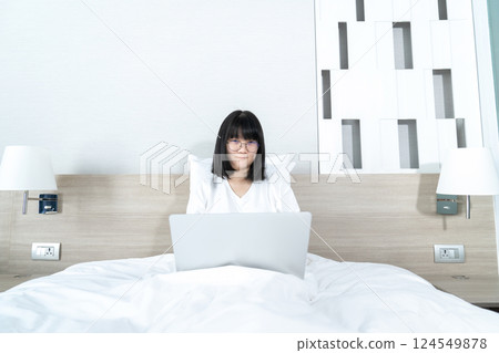 Glasses Asian cute woman works and plays laptop notebook on the bed in Work From Home period. 124549878