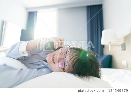 Asian young glasses woman talk to the mobile phone while lie on her side on the bed in the morning. 124549879