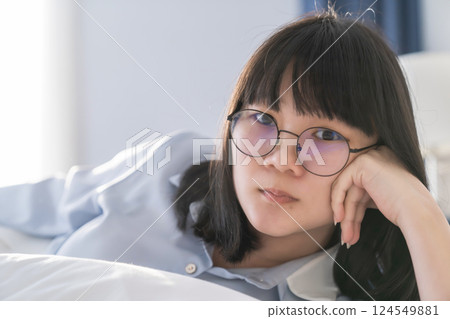 Asian young glasses woman lie on her side on the bed in the morning. 124549881