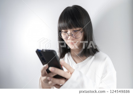 Isolated Pretty Asian glasses woman looks and holds mobile phone in her hand on white background in studio light. 124549886