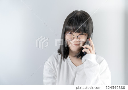 Isolated Pretty Asian glasses woman talks and speaks in the line with her mobile phone on white background in studio light. Isolated Pretty Asian glasses woman talks and speaks in the line with her mobile phone on white background in studio light. 124549888
