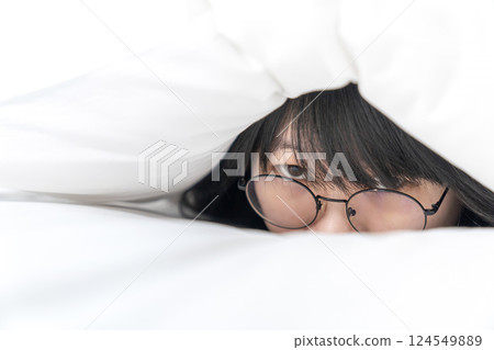 close up to the Cute Asian Glasses woman, she hides her body inside white pillow on the bed 124549889