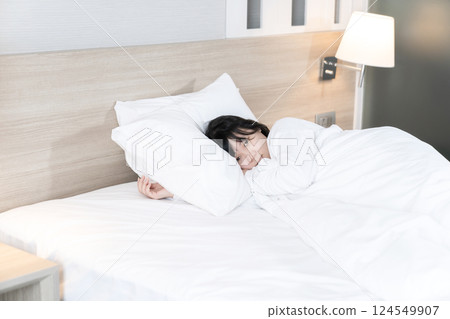 Asian cute young woman in white long arm pajamas lie on her side on the bed and her eyes look to the camera 124549907