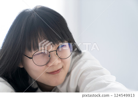 Winked glasses sweet, cute Asian girl lays on the bed with happy and comfort feeling in front of window light in the morning. 124549913