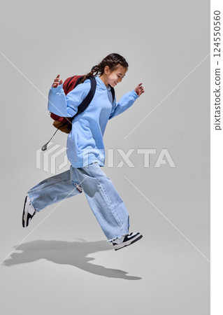 Girl with backpack joyfully leaps forward, ready for new adventures and knowledge awaiting on back to school day. Education concept. Girl with backpack joyfully leaps forward, ready for new adventures and knowledge awaiting on back to school day. Education concept. 124550560