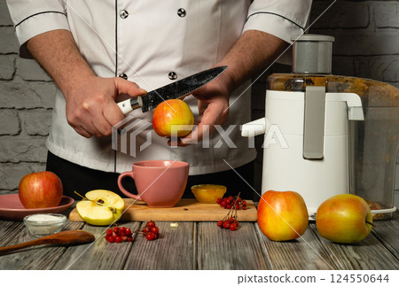 Slicing apples with a knife to make fresh juice with an electric juicer in the kitchen. Making a healthy apple drink for breakfast. Concept for an apple diet menu Slicing apples with a knife to make fresh juice with an electric juicer in the kitchen. Making a healthy apple drink for breakfast. Concept for an apple diet menu 124550644