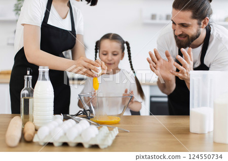 Caucasian family showing father, mother, and young daughter cooking meal in kitchen setting. Family bonding, cooking, and culinary learning captured with enthusiasm, teamwork, and togetherness. Caucasian family showing father, mother, and young daughter cooking meal in kitchen setting. Family bonding, cooking, and culinary learning captured with enthusiasm, teamwork, and togetherness. 124550734