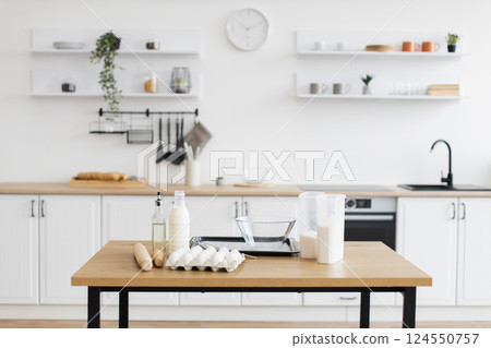 Bright contemporary kitchen containing minimalist decor and baking essentials such as eggs, milk, and flour on table, emphasizing simplicity and readiness for cooking or baking. 124550757