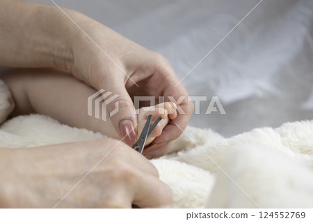 Mom trims baby's nails with baby scissors. Close up photo of mother's hands holding feet of the infant and nail scissors. 124552769