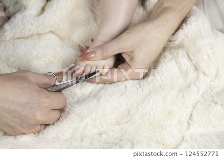 Mom trims baby's nails with baby scissors. Close up photo of mother's hands holding feet of the infant and nail scissors. Mom trims baby's nails with baby scissors. Close up photo of mother's hands holding feet of the infant and nail scissors. 124552771