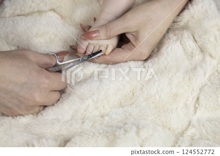 Mom trims baby's nails with baby scissors. Close up photo of mother's hands holding feet of the infant and nail scissors. 124552772