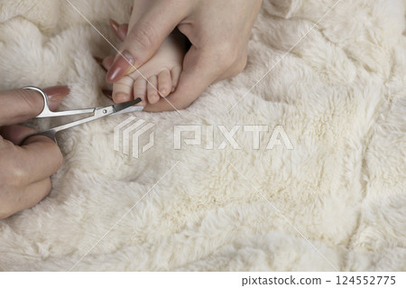 Mom trims baby's nails with baby scissors. Close up photo of mother's hands holding feet of the infant and nail scissors. Mom trims baby's nails with baby scissors. Close up photo of mother's hands holding feet of the infant and nail scissors. 124552775