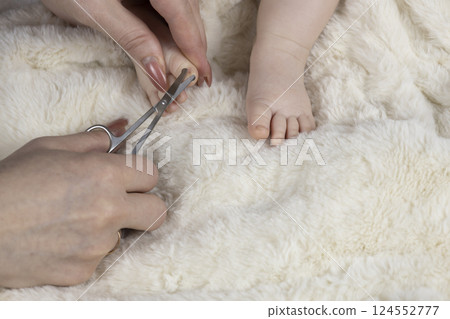 Mom trims baby's nails with baby scissors. Close up photo of mother's hands holding feet of the infant and nail scissors. 124552777