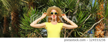 Summer beautiful young woman posing in straw tourist hat standing in park with palm trees Summer beautiful young woman posing in straw tourist hat standing in park with palm trees 124553236