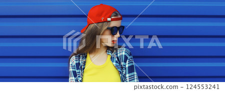 Stylish young girl in baseball cap, glasses, modern teenager girl posing on blue wall background 124553241