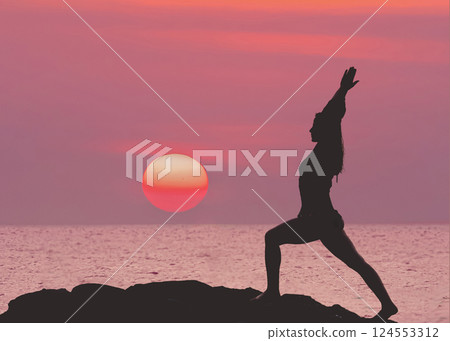 Yoga tour by the sea. Silhouette of a woman in yoga pose on a rock in close-up, against the background of a purple red sunset with a red big sun. 124553312