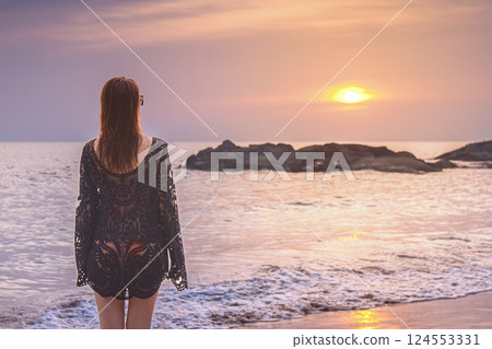 Solo Travel. A woman in a black cape looks at the sea sunset on the beach in Khao Lak, Thailand. Solo Travel. A woman in a black cape looks at the sea sunset on the beach in Khao Lak, Thailand. 124553331