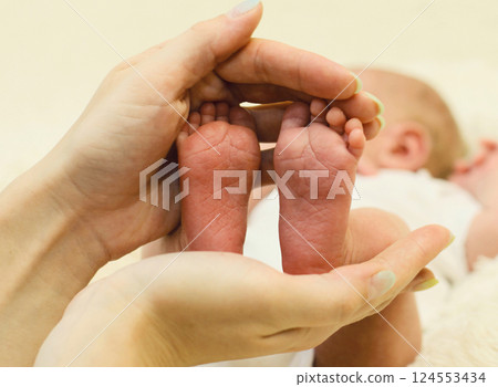 Mother holding in her hands baby feet close up lying on the bed 124553434