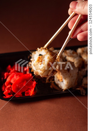 Hand with chopsticks taking portion of sushi roll. Sushi rolls with salmon cream cheese and cucumber in take away package. Food delivery concept. Hand with chopsticks taking portion of sushi roll. Sushi rolls with salmon cream cheese and cucumber in take away package. Food delivery concept. 124554003
