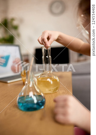 Close-up of child hands conducting home chemistry experiment following instructions from online science video. 124554408