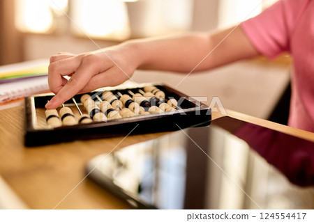 Closeup of child hand moving beads on abacus next to digital tablet and school supplies during home learning. Counting. Closeup of child hand moving beads on abacus next to digital tablet and school supplies during home learning. Counting. 124554417