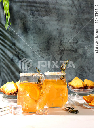 Summer party concept. Tequila, rum and vodka cocktail with pineapple slices, orange, ice and rosemary. Diet drink for detoxification and weight loss, bar or cafe advertisement, restaurant menu Summer party concept. Tequila, rum and vodka cocktail with pineapple slices, orange, ice and rosemary. Diet drink for detoxification and weight loss, bar or cafe advertisement, restaurant menu 124554742