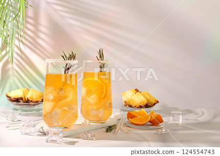 Summer party concept. Tequila, rum and vodka cocktail with pineapple slices, orange, ice and rosemary. Diet drink for detoxification and weight loss, bar or cafe advertisement, restaurant menu 124554743