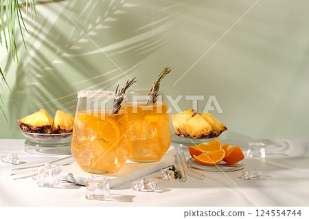 Tequila, rum and vodka cocktail with pineapple slices, orange, ice and rosemary. Summer party concept. Diet drink for detoxification and weight loss, bar or cafe advertisement, restaurant menu 124554744