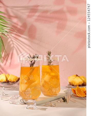Tequila, rum and vodka cocktail with pineapple slices, orange, ice and rosemary. Summer party concept. Diet drink for detoxification and weight loss, bar or cafe advertisement, restaurant menu Tequila, rum and vodka cocktail with pineapple slices, orange, ice and rosemary. Summer party concept. Diet drink for detoxification and weight loss, bar or cafe advertisement, restaurant menu 124554747