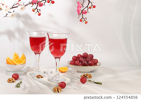 Glasses of red wine, red grapes and citrus slices on elegant background with spring sakura flowers, bar and summer party concept, restaurant and cafe advertising card, selective focus 124554856