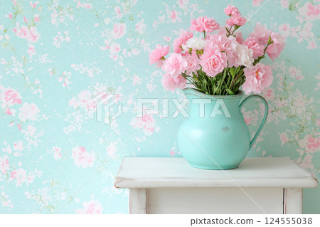 A pastel-themed image of pink flowers in a blue pitcher, complemented by a matching floral wallpaper. Perfect for evoking feelings of nostalgia and warmth with a shabby chic vintage aesthetic. 124555038