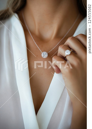 Elegant woman showcasing diamond necklace matching sparkling engagement ring. Close-up of elegance, sparkling jewelry including necklace and a diamond ring. Luxury jewelry 124555082