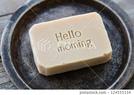 A handcrafted bar of soap embossed with "Hello Morning", evoking a sense of freshness and natural beauty, photographed with an artistic and rustic aesthetic. 124555134