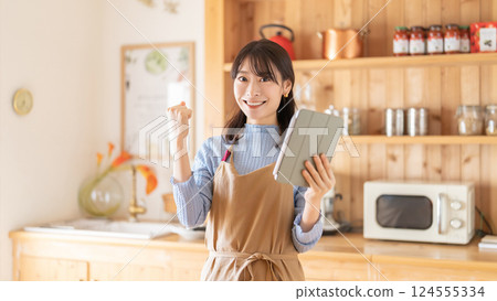 A smiling woman cooking while looking at a tablet 124555334
