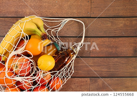 Lemons, oranges, tomatoes, apples, bananas and natural juice in a reusable bag, Fabric string bag with healthy vegan products for weight loss. food delivery concept, store advertising 124555668