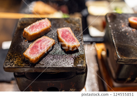 Gyukatsu slices cooking on a tabletop ceramic grill with sizzling juices and a golden-brown crust 124555851