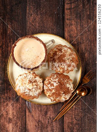 Chocolate muffins with nutmeg and cinnamon eggnog on a wooden background, cozy breakfast concept, advertising for a cafe or bakery. Warming egg drink in cold season with delicious dessert, selective Chocolate muffins with nutmeg and cinnamon eggnog on a wooden background, cozy breakfast concept, advertising for a cafe or bakery. Warming egg drink in cold season with delicious dessert, selective 124556250