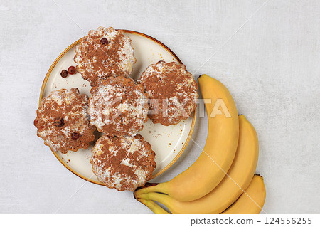 Delicious banana muffins with cocoa on a concrete kitchen table and bananas, healthy diet food. Advertising card or menu for a cafe, restaurant. Concept of a modern bakery, selective focus. Delicious banana muffins with cocoa on a concrete kitchen table and bananas, healthy diet food. Advertising card or menu for a cafe, restaurant. Concept of a modern bakery, selective focus. 124556255