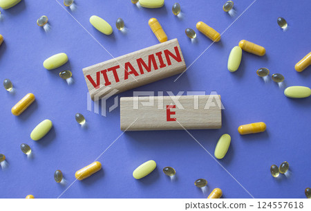 Vitamin E symbol. Concept word Vitamin E on wooden blocks. Beautiful purple background with pills. Medicine and Vitamin E concept. Copy space Vitamin E symbol. Concept word Vitamin E on wooden blocks. Beautiful purple background with pills. Medicine and Vitamin E concept. Copy space 124557618